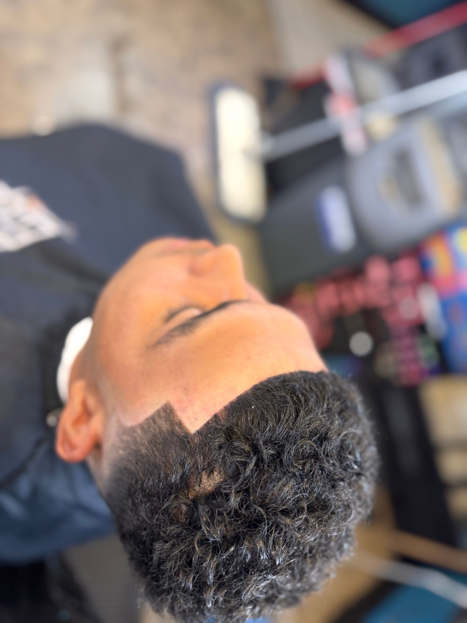 A man with curly hair is laying on his back in a barber shop.