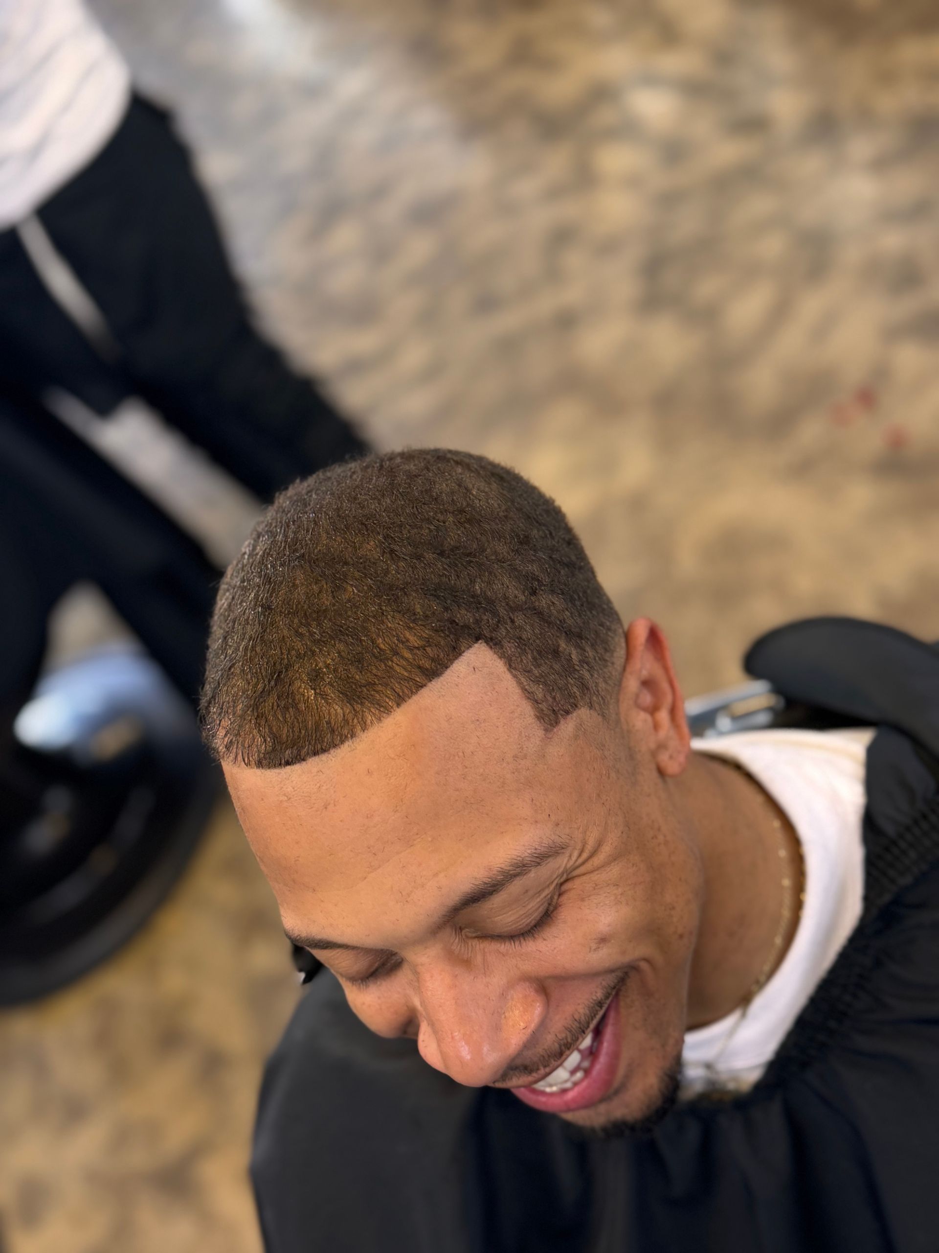 A man is smiling while getting his hair cut at a barber shop