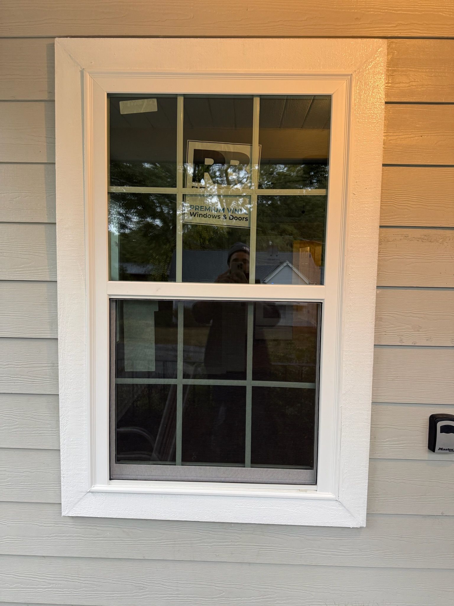 White-framed window on a light gray house. Reflecting outdoors, with dark mullions and a white trim surround.