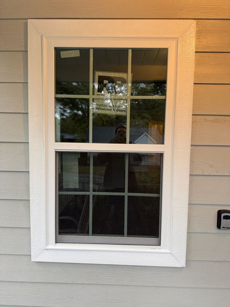 White-framed window on a light gray house. Reflecting outdoors, with dark mullions and a white trim surround.