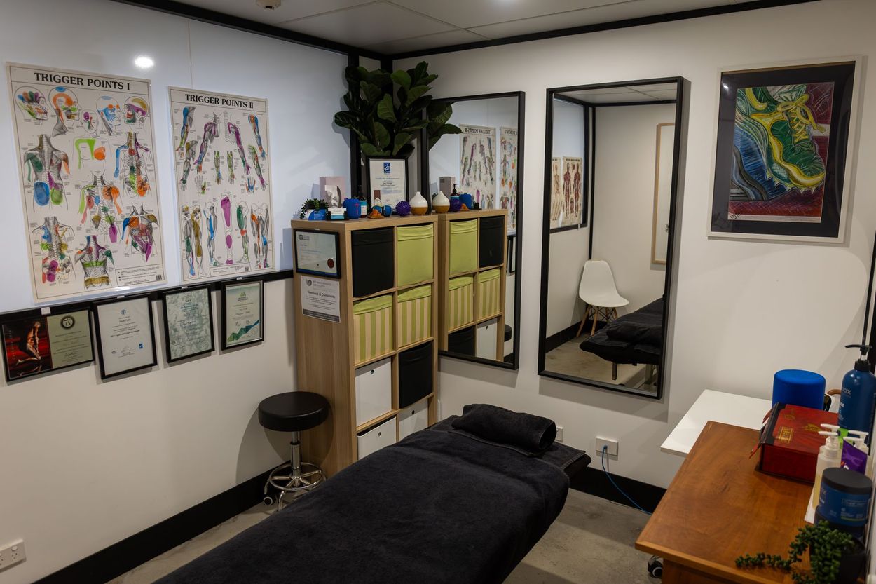 Massage therapy room with a massage table, storage, mirrors, anatomy posters, and art.