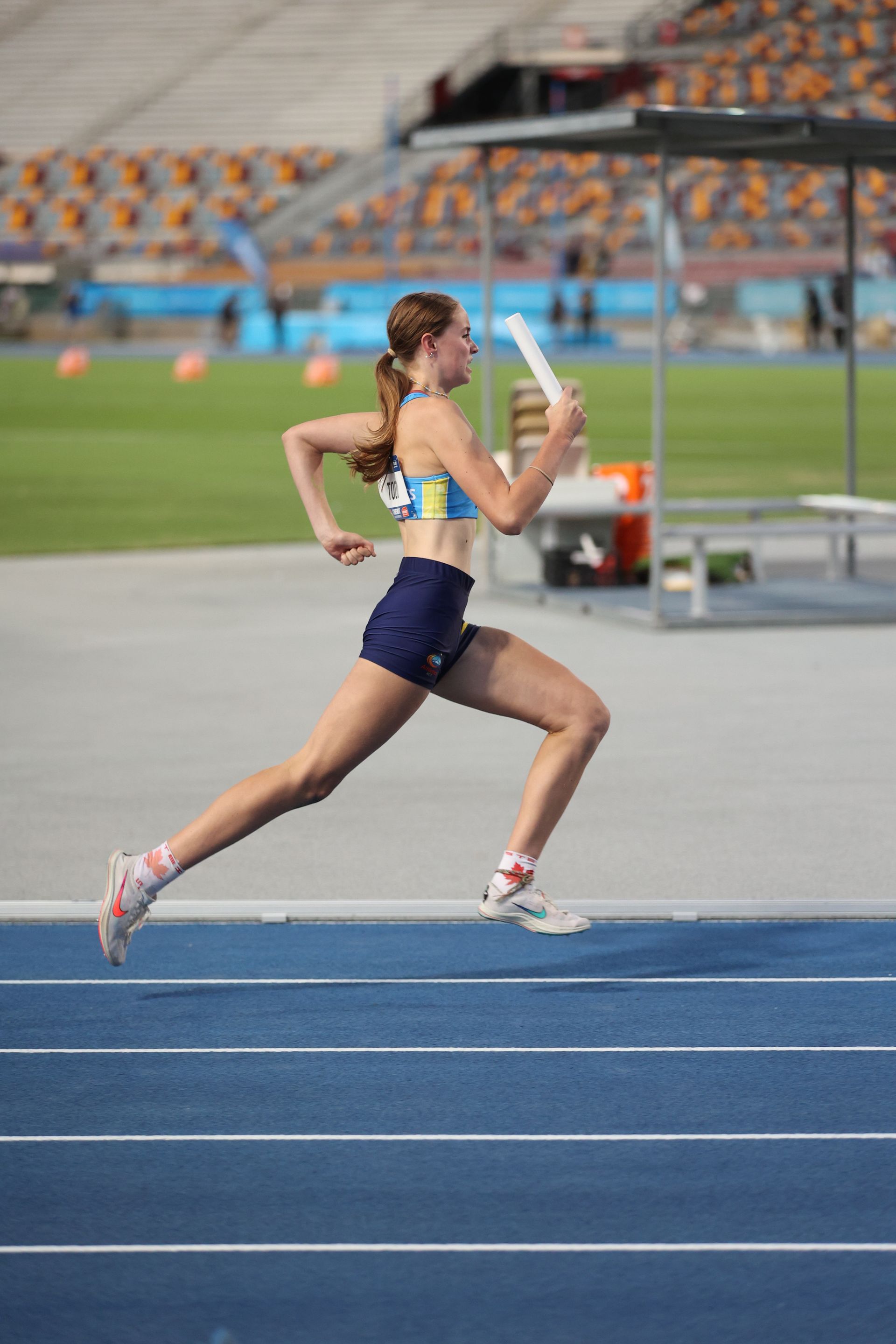 A woman is running on a track holding a relay baton.