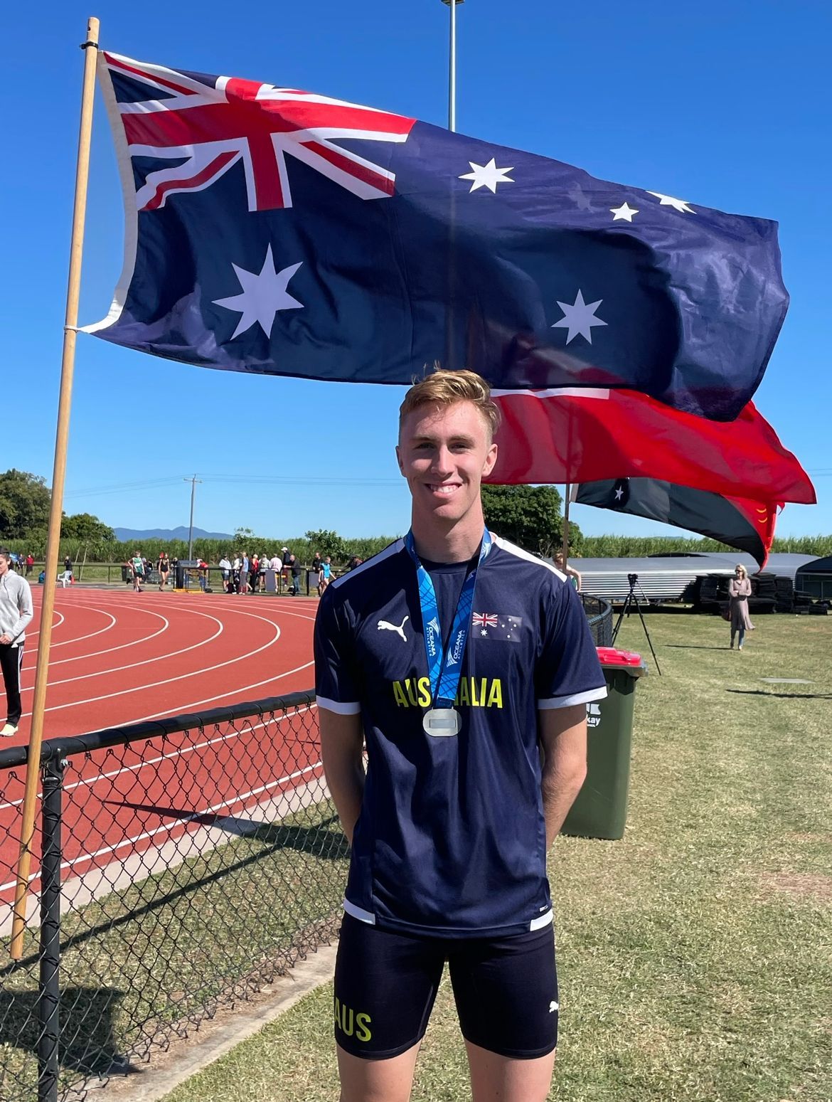 A young man is standing in front of an australian flag on a track.