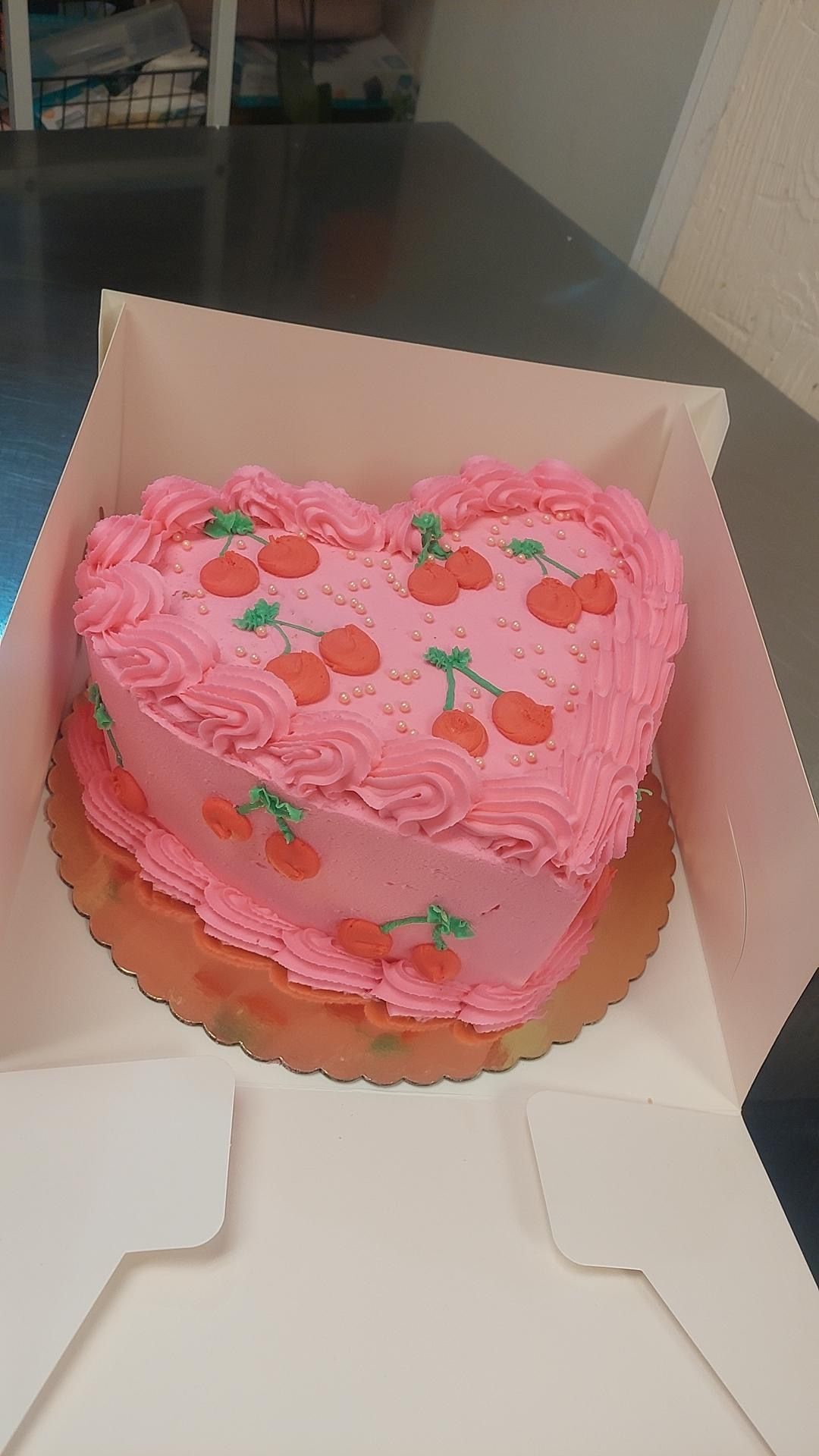 A heart shaped cake with cherries on it is in a box.