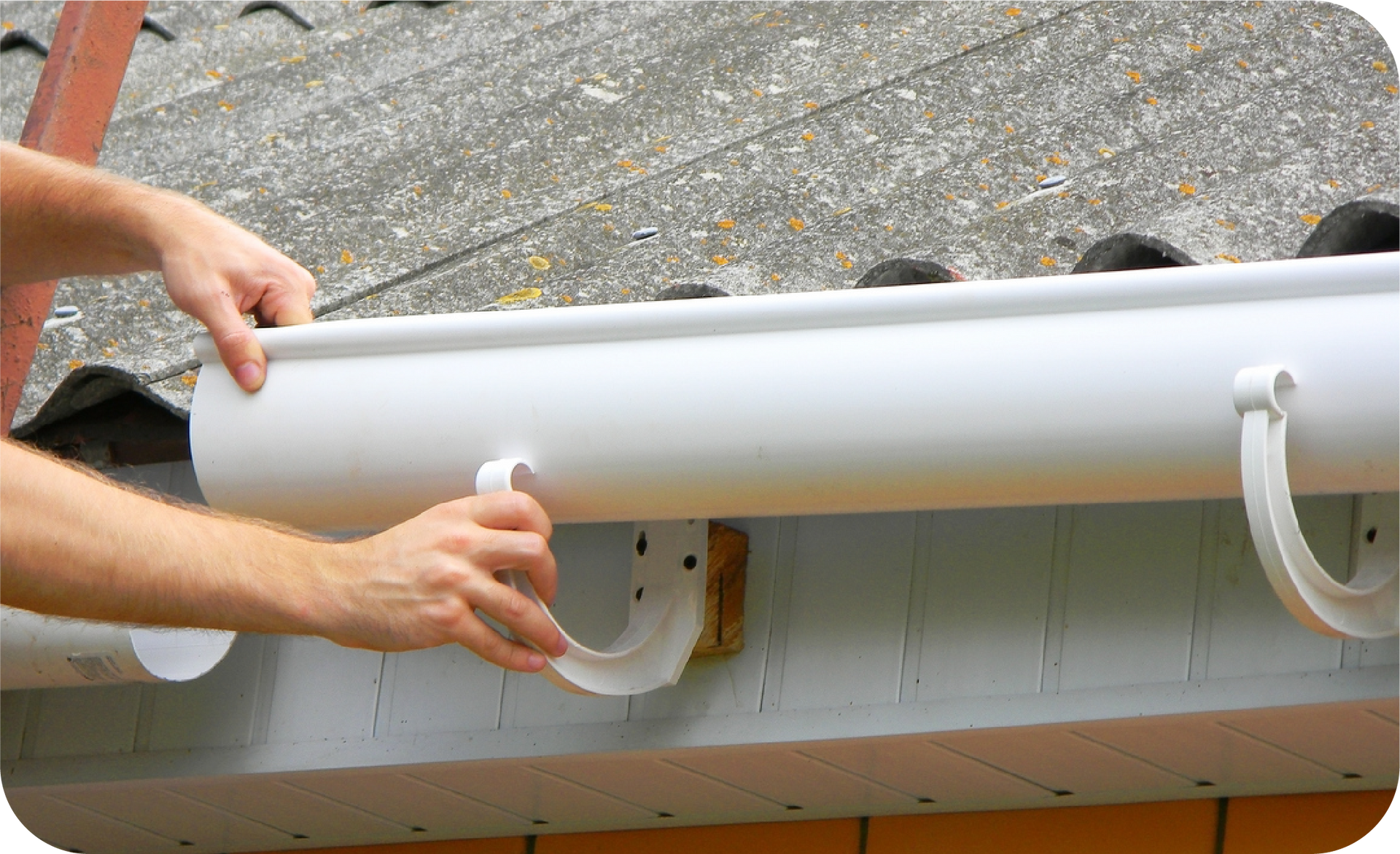 A person installing a white gutter section on a roof.