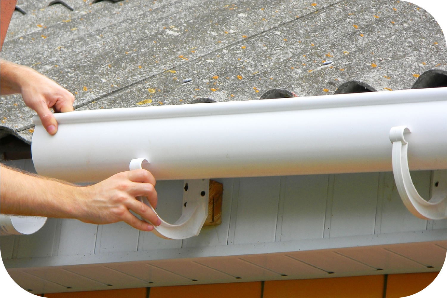 Hands installing white gutter section onto a bracket attached to a house.