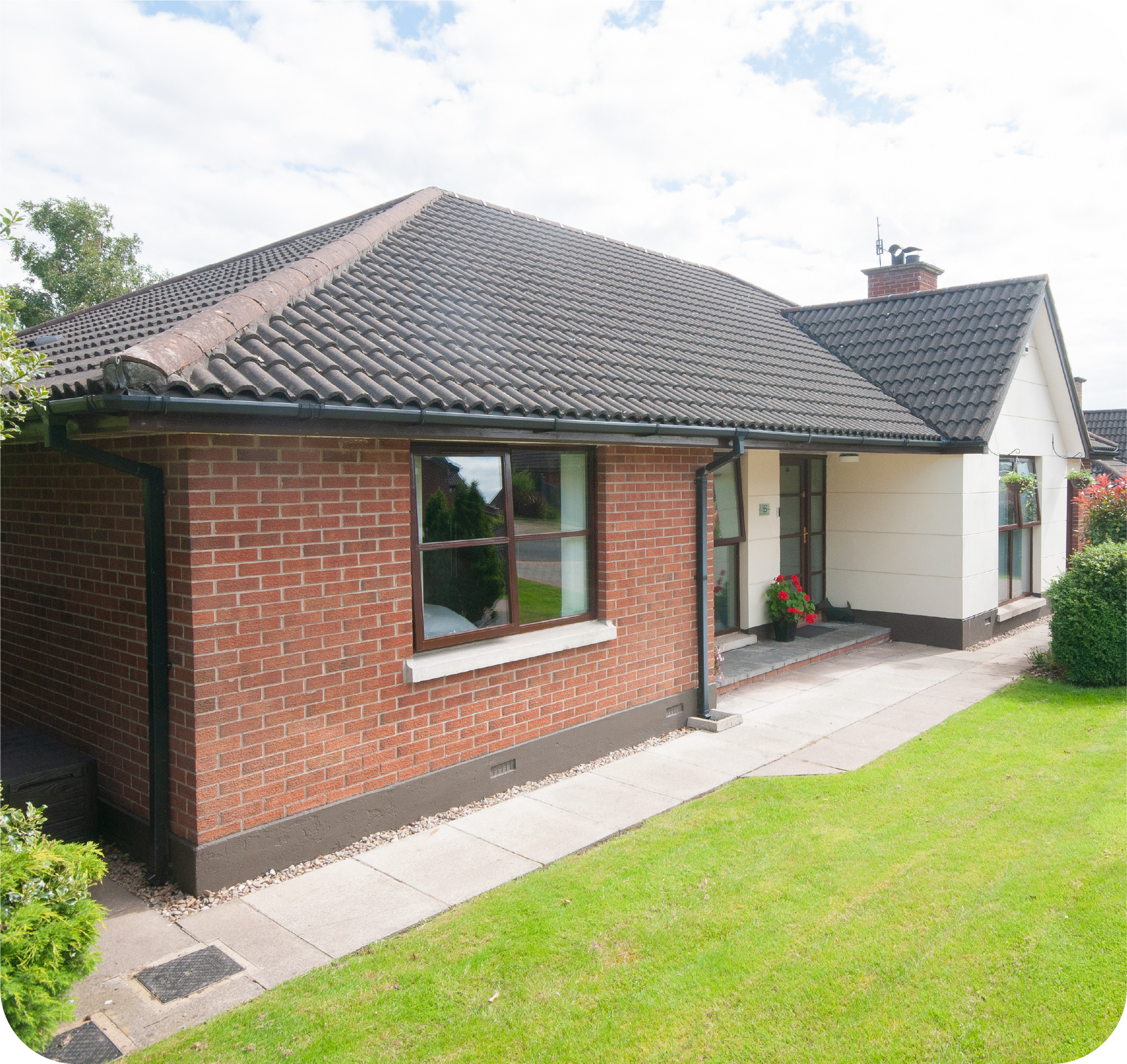 Brick bungalow with a dark tiled roof, a walkway, and green grass.