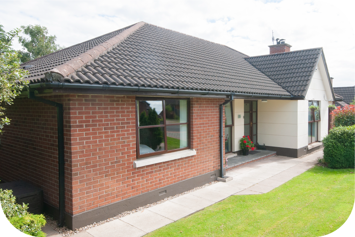 Red brick bungalow with dark roof and trim, front porch, and green lawn.
