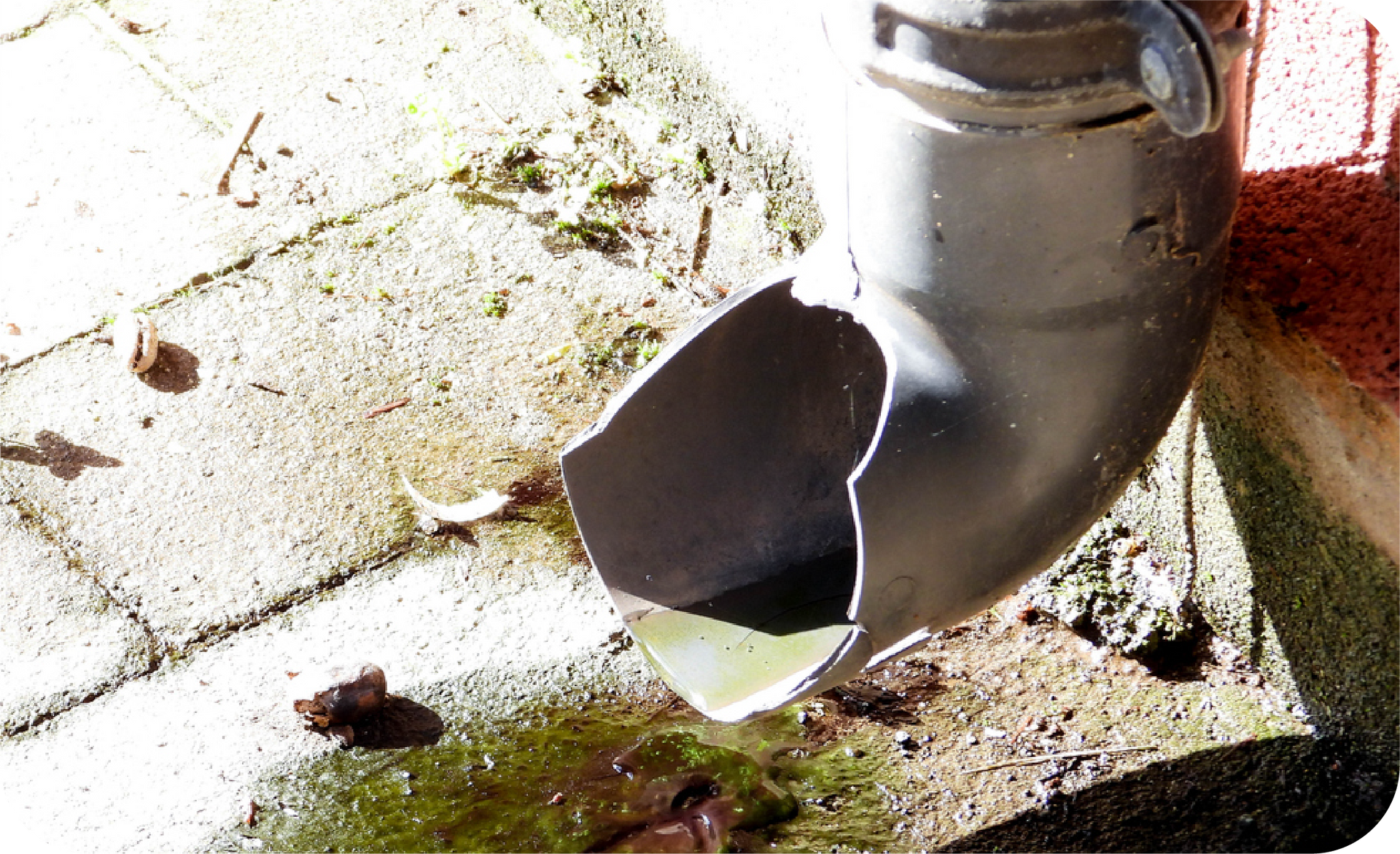 Damaged gray downspout leaking water onto a brick surface.