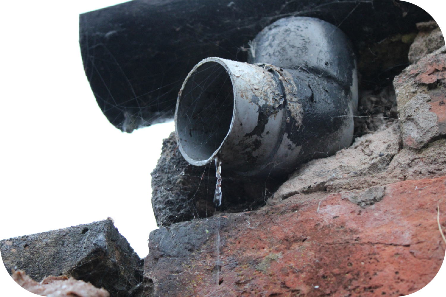 Leaking pipe elbow emerging from brickwork, with dripping water.