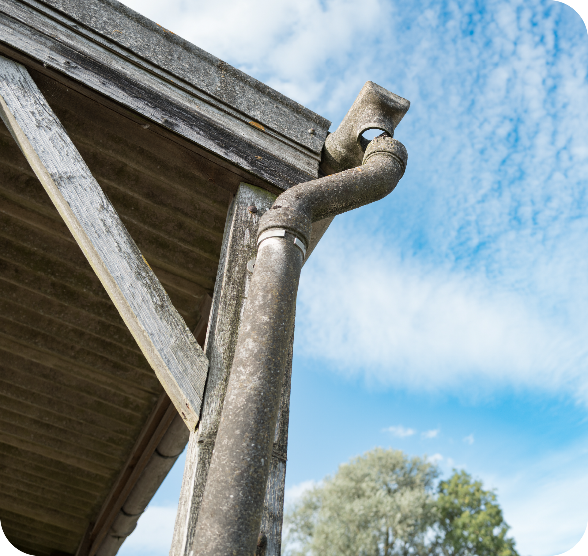 Gutter and downspout on a wooden structure, against a blue sky with clouds.
