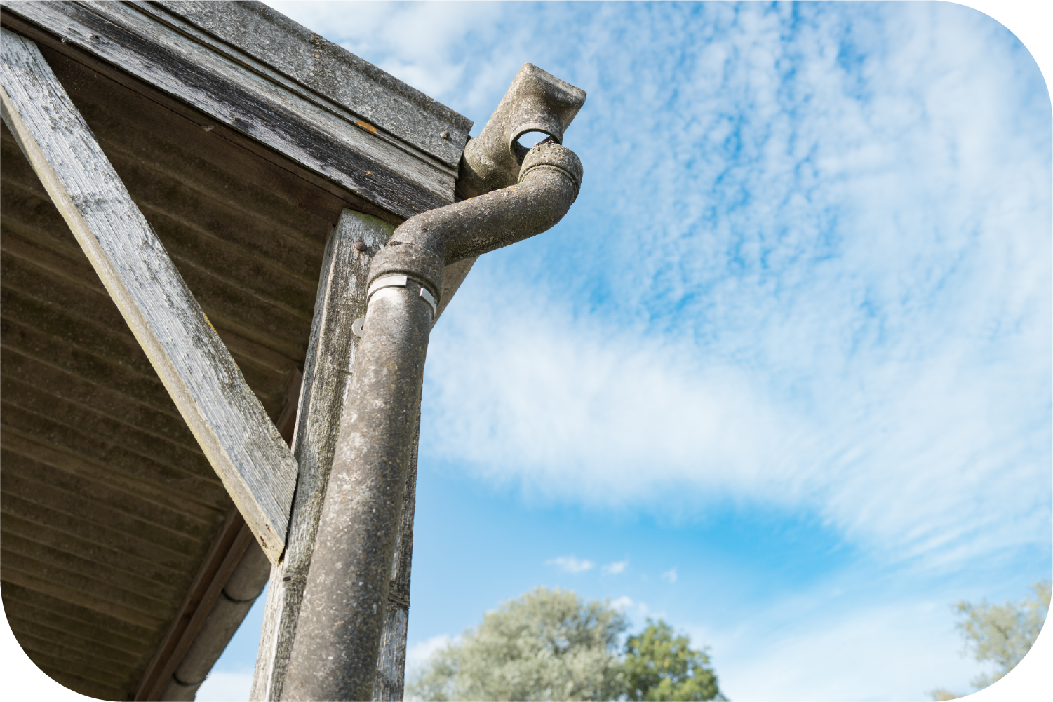 Weathered concrete gutter system on a wooden structure, blue sky in the background.