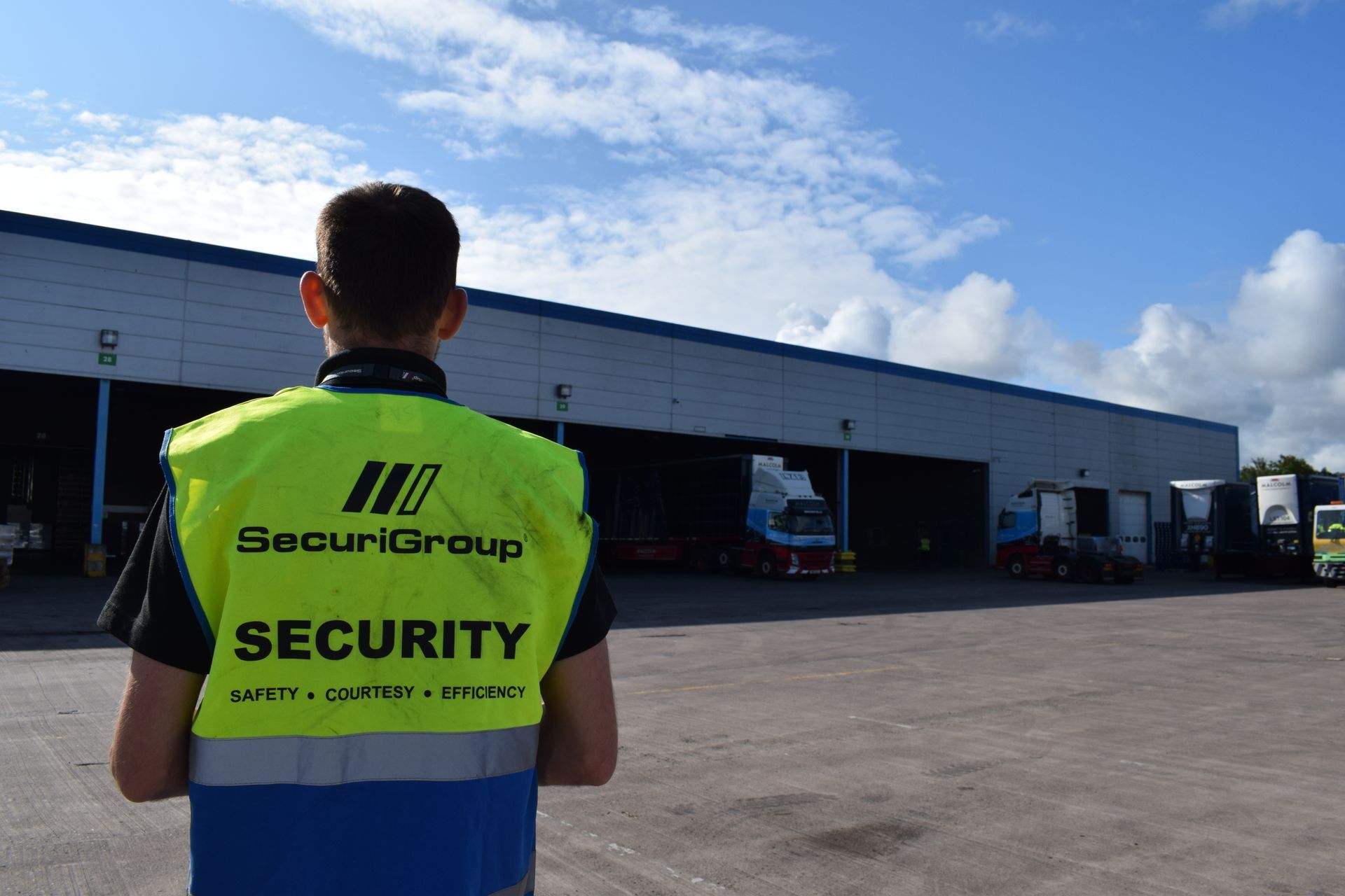 A man wearing a security vest is standing in front of a building.