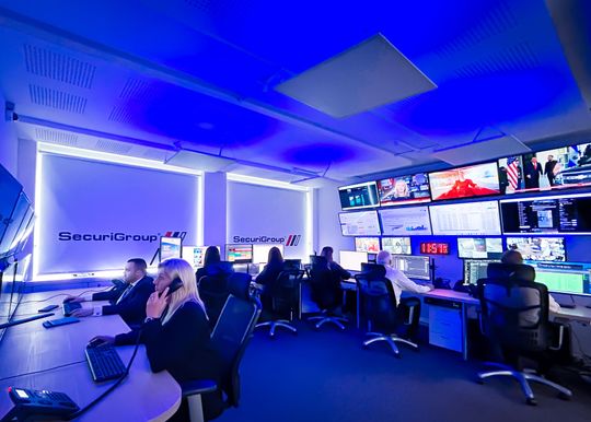 A group of people are sitting at desks in a control room.