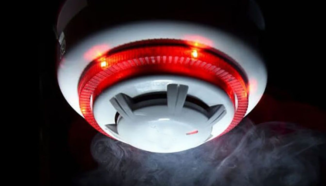 Smoke detector with a flashing red light, emitting smoke in a dark environment.