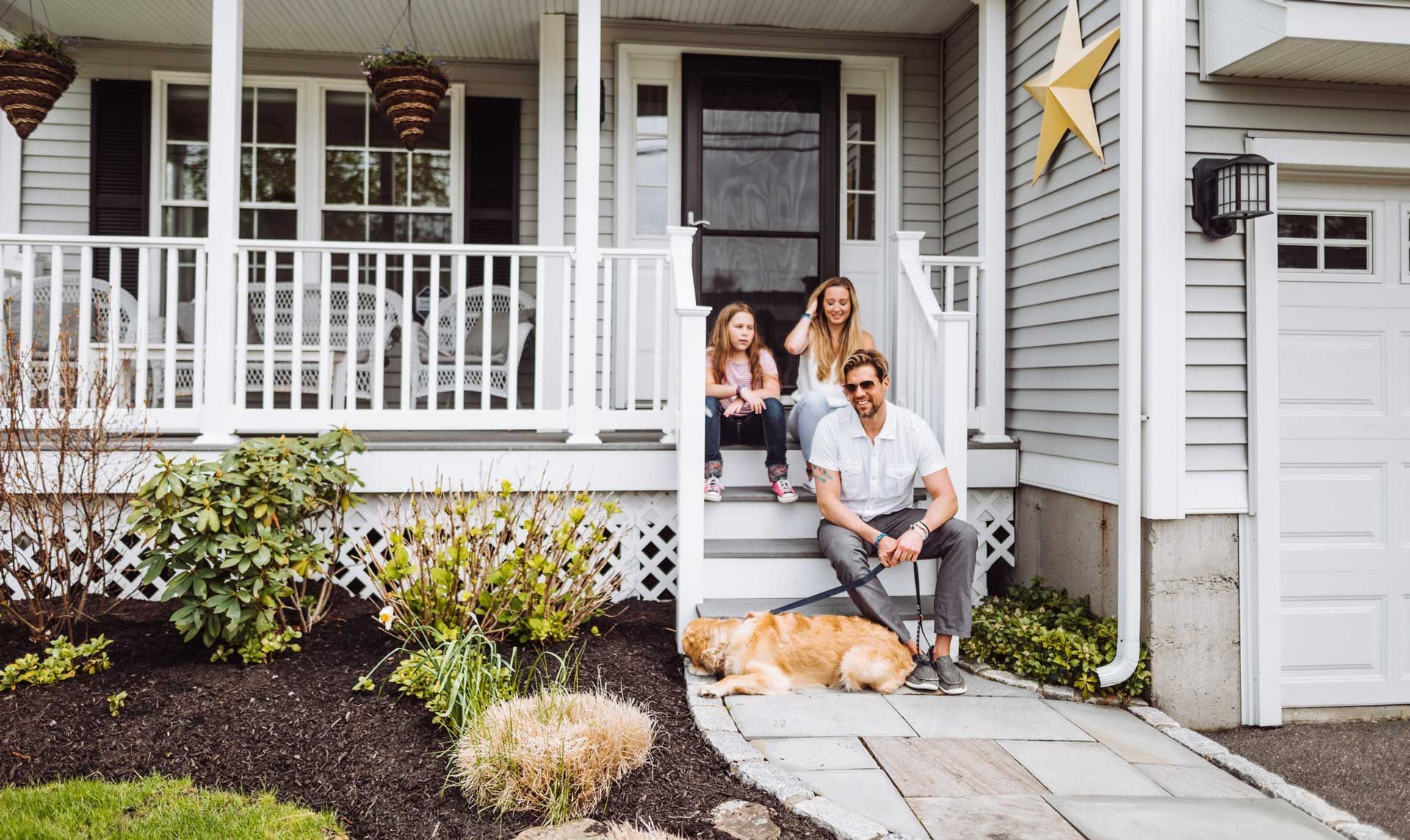A family is sitting on the porch of their house with a dog.