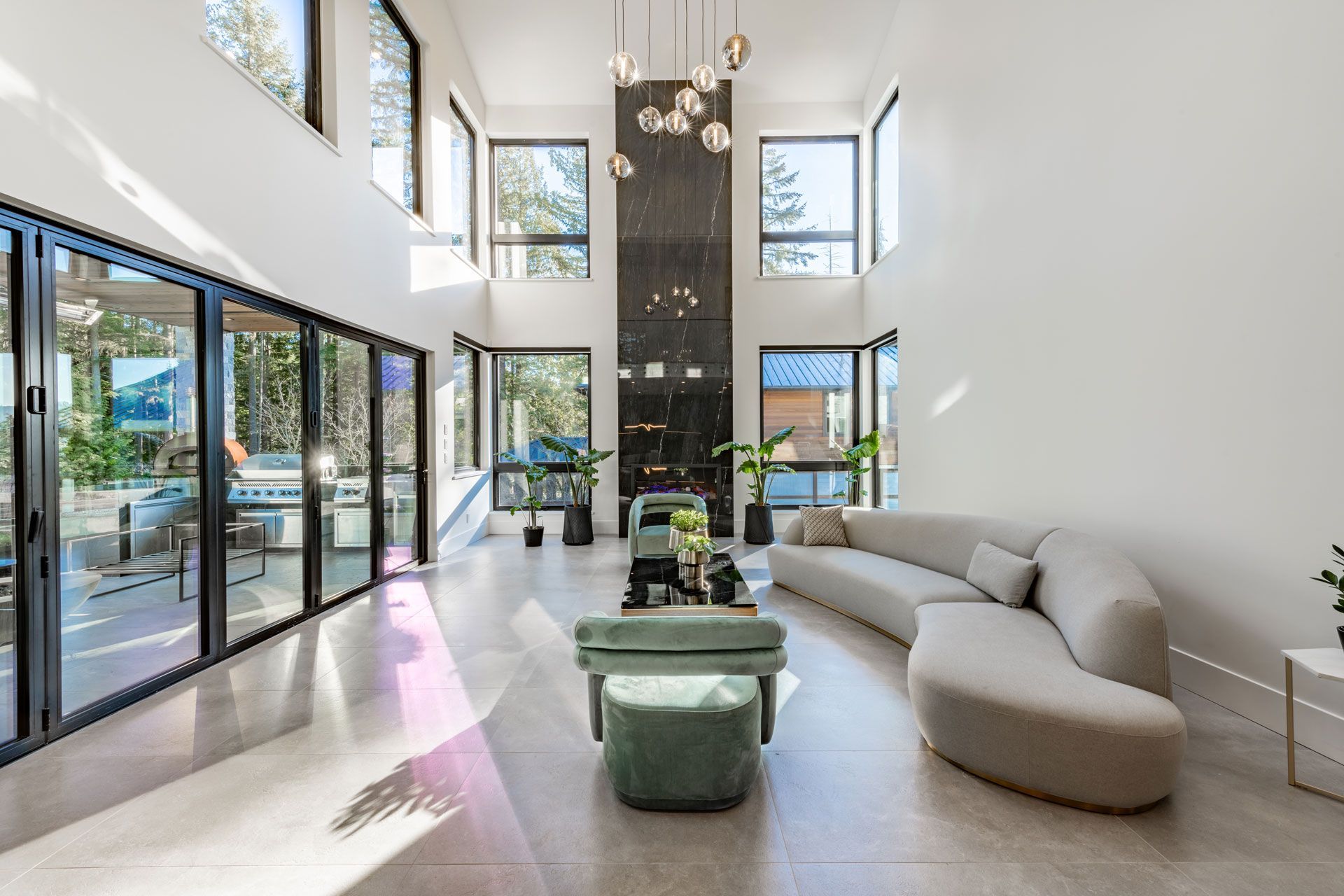 Bright modern living room with tall windows, white walls, and a curved beige sofa beside green ottomans.