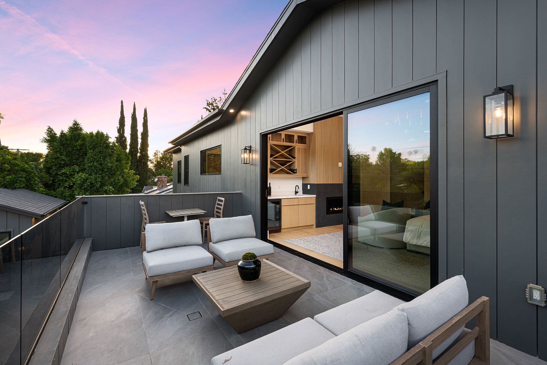 Modern rooftop patio with gray outdoor seating, fire pit table, and sliding glass doors at sunset