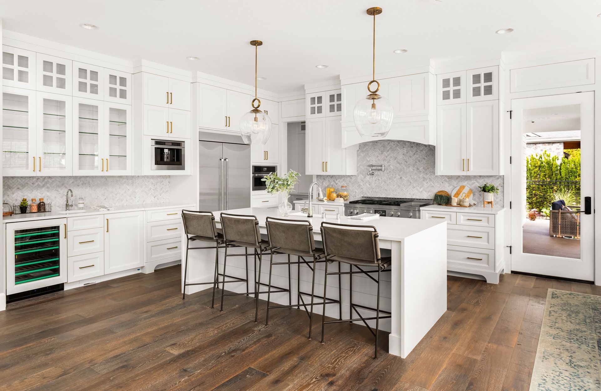 Bright white modern kitchen with island, bar stools, wood floors, and a doorway to the outdoors
