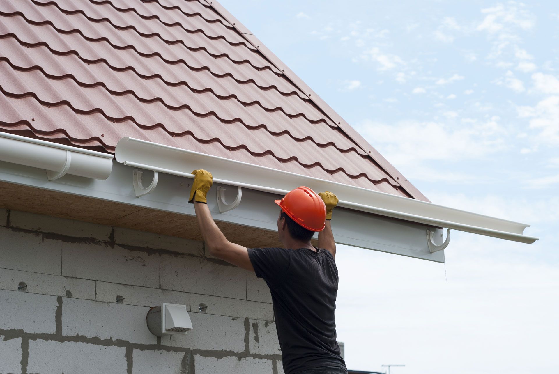 Worker in orange hard hat applying sealant to the edge of a red-tiled roof