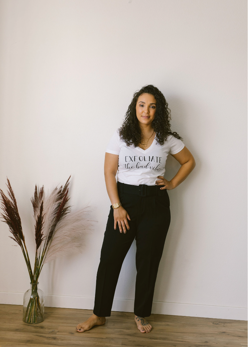 A woman in a white t-shirt and black pants is standing next to a vase of flowers.