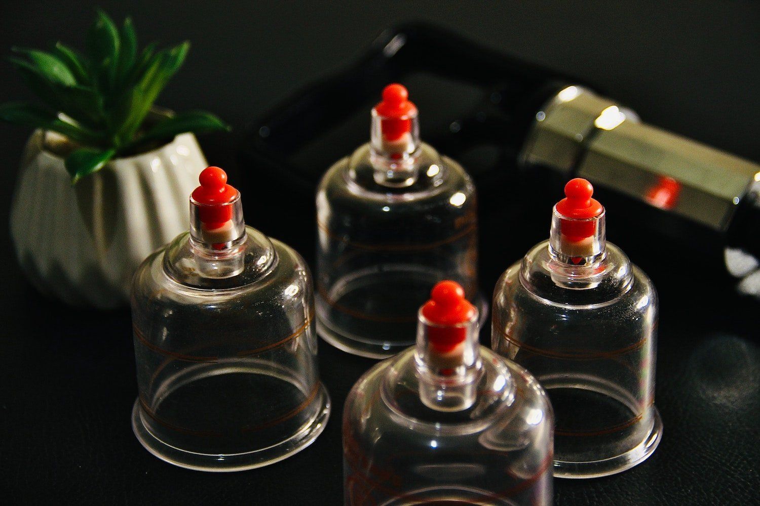 Four clear cups with red caps are sitting on a table next to a plant.