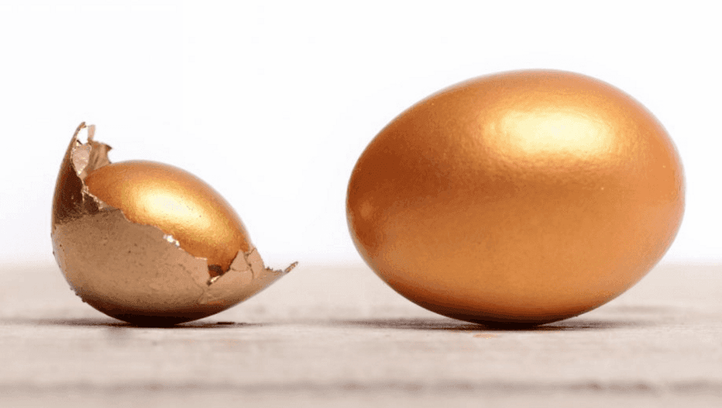 Close up shot of the top of a cracked golden egg shell and a fully intact golden egg