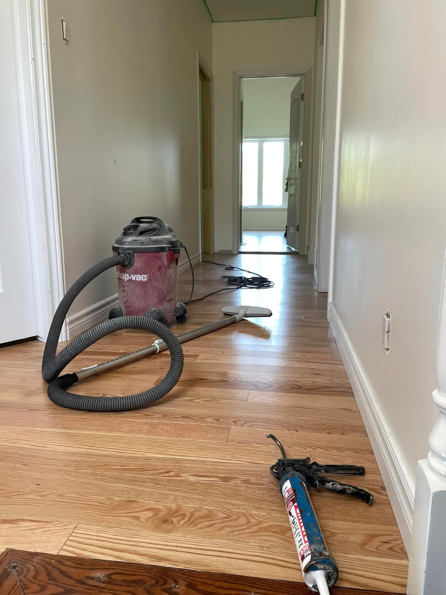 Un aspirateur est posé sur un plancher en bois dans un couloir.