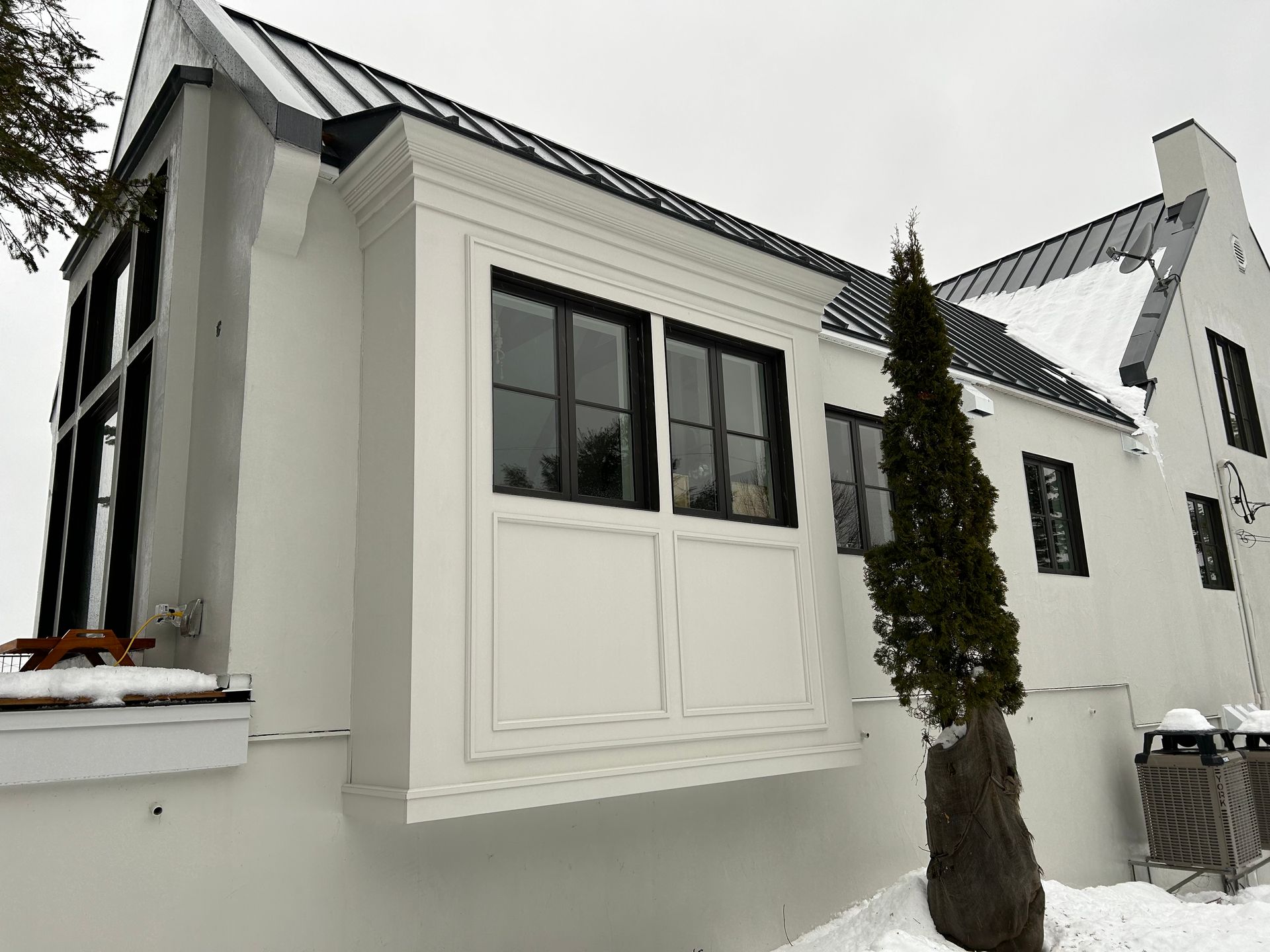 Une maison blanche avec des fenêtres noires et une grande baie vitrée.