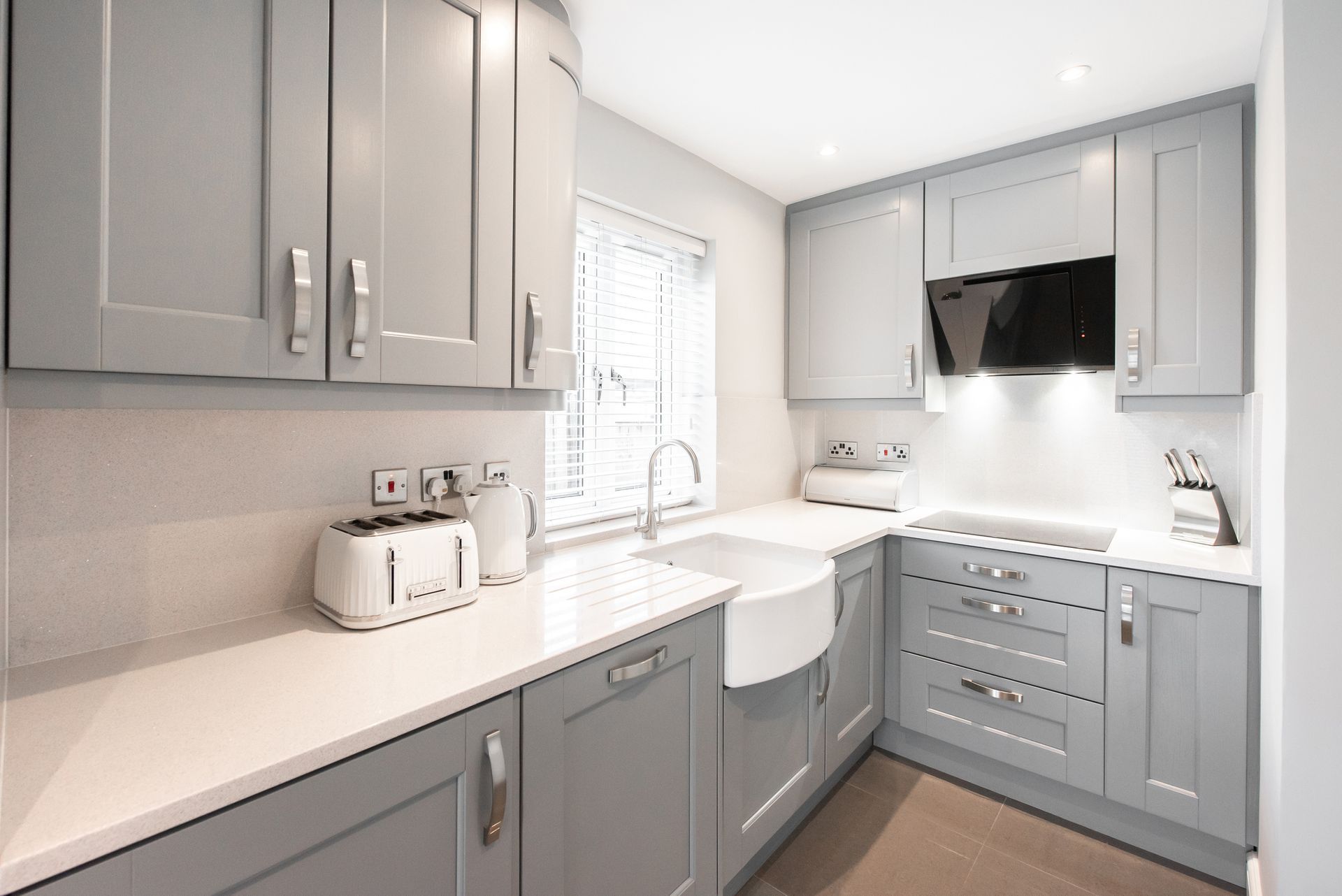 A kitchen with gray cabinets , white counter tops , a sink and a toaster oven.