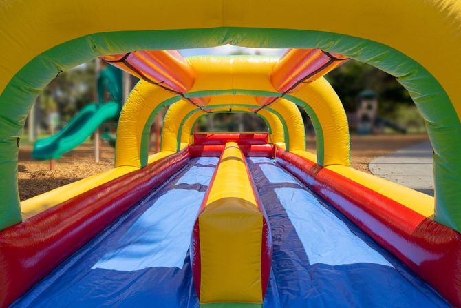 Colorful inflatable slide with red, yellow, and blue lanes at an outdoor playground