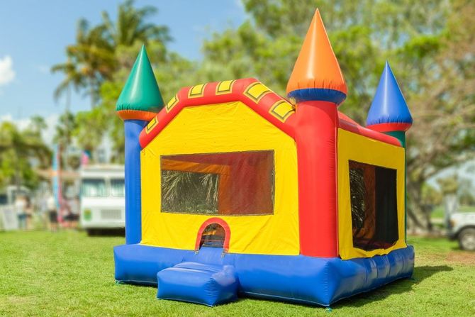 Colorful inflatable bounce house on grass, with red, yellow, blue, and green turrets in a sunny park