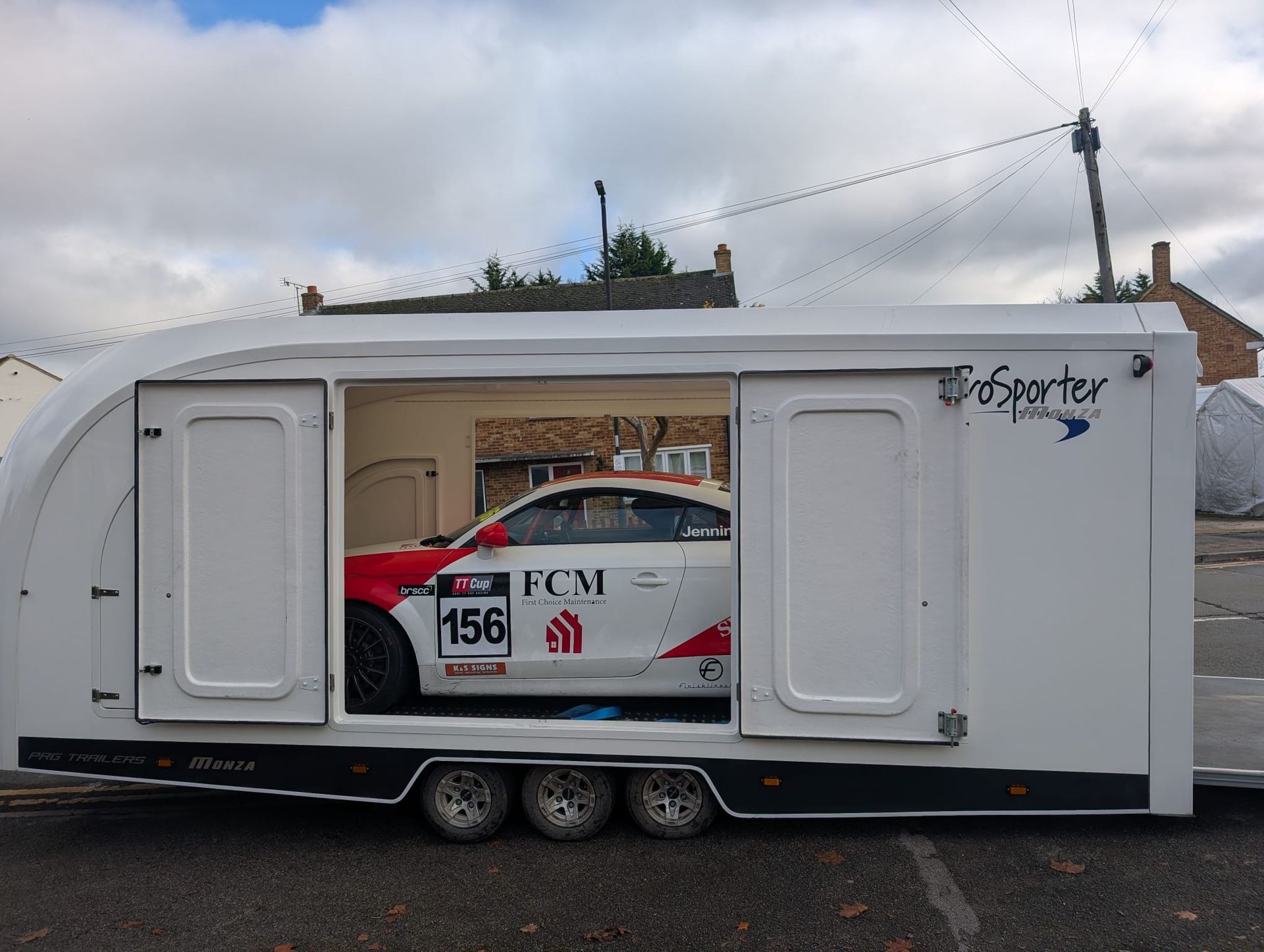 White trailer with an open side, revealing a race car inside.