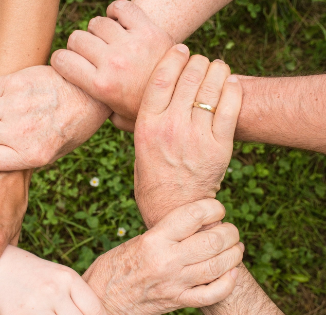 Plusieurs mains empilées les unes sur les autres en cercle, se détachant sur un fond d'herbe verte.