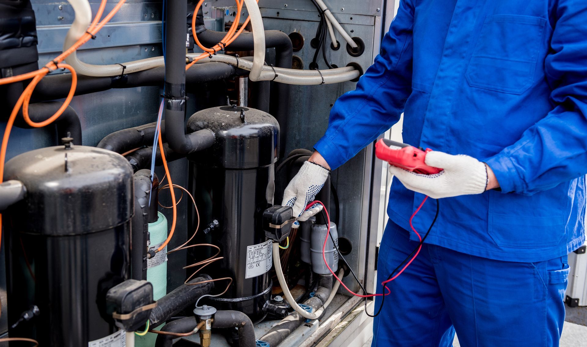 HVAC technician in blue uniform using a multimeter.