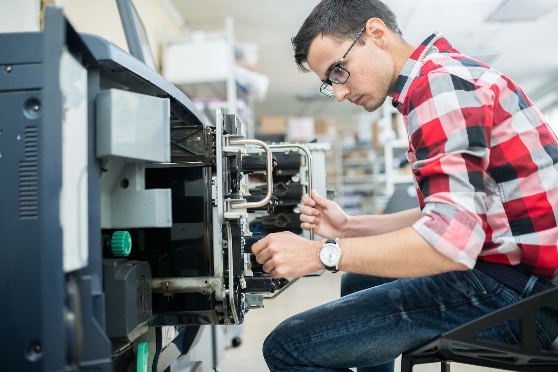 Man in plaid shirt fixing machinery, inside.