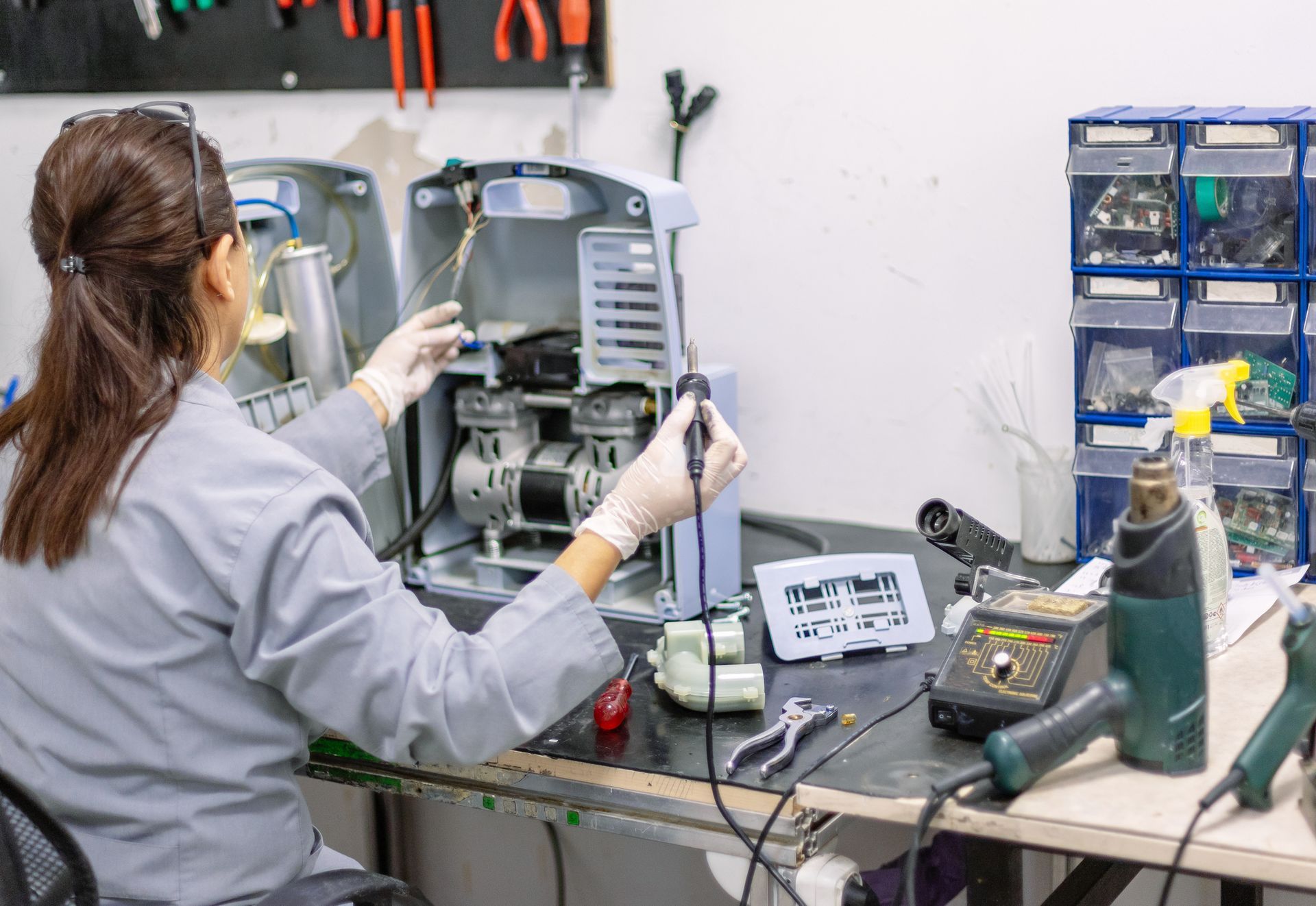 Woman in gloves repairing a machine in a workshop.