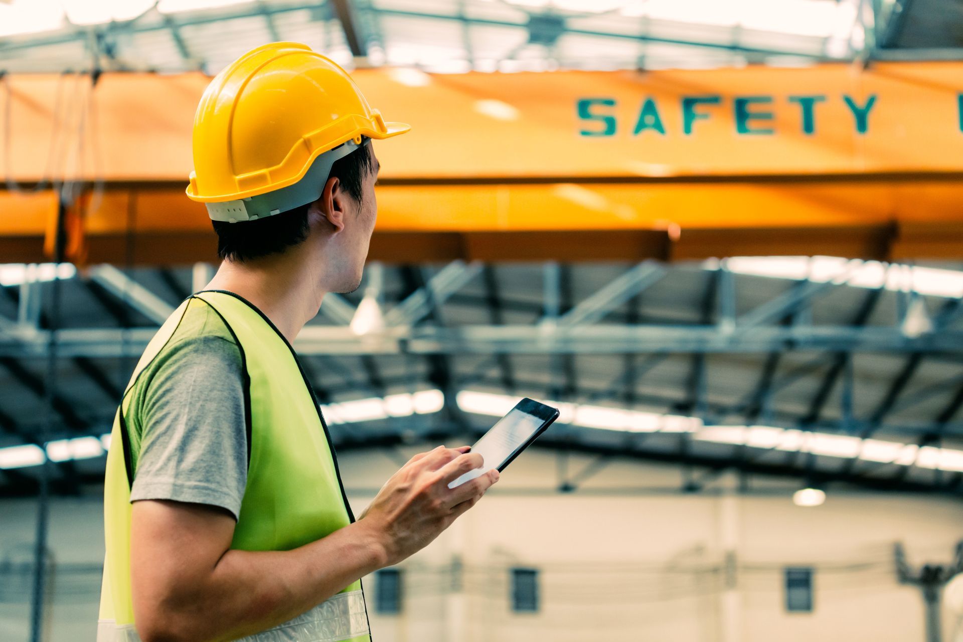 Construction worker in hardhat and safety vest using a tablet in a factory..