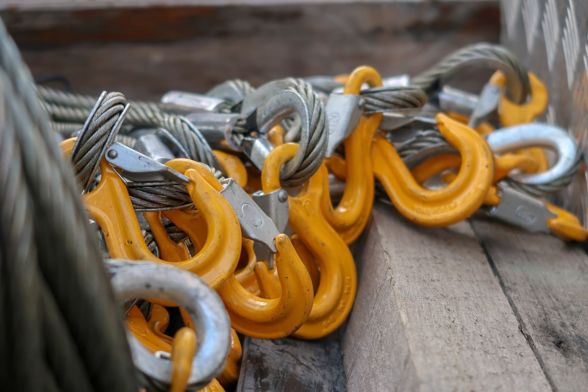 Yellow and silver metal hooks and cables piled in a wooden container.