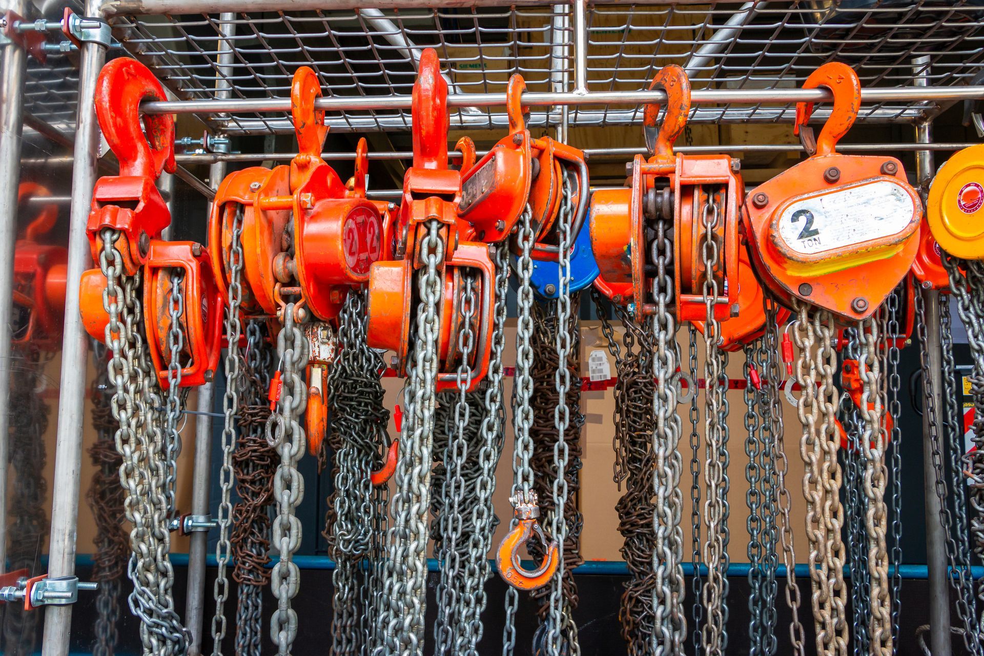 Row of orange industrial pulley hoists with hanging metal chains.
