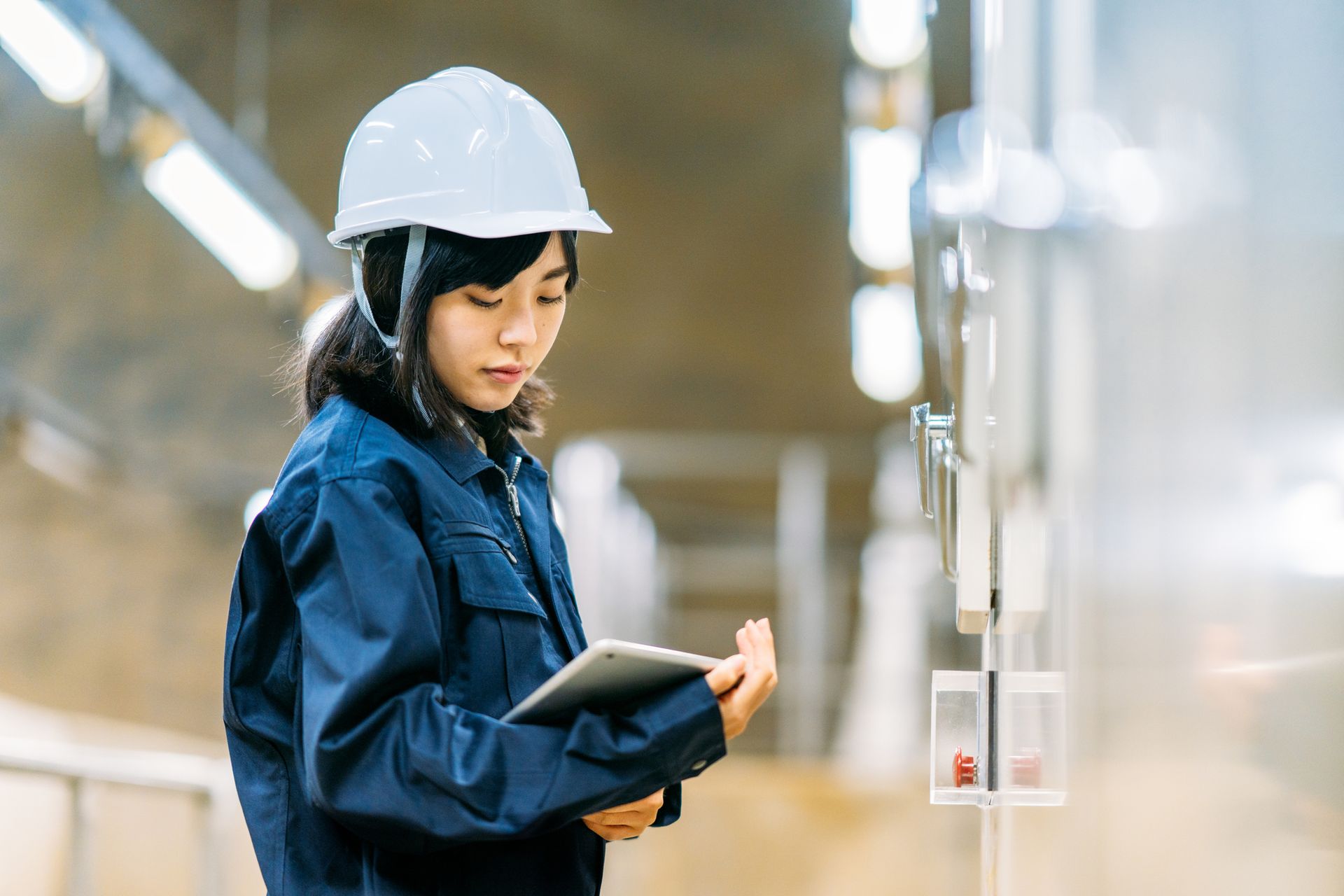 Woman in hard hat and work uniform uses a tablet.