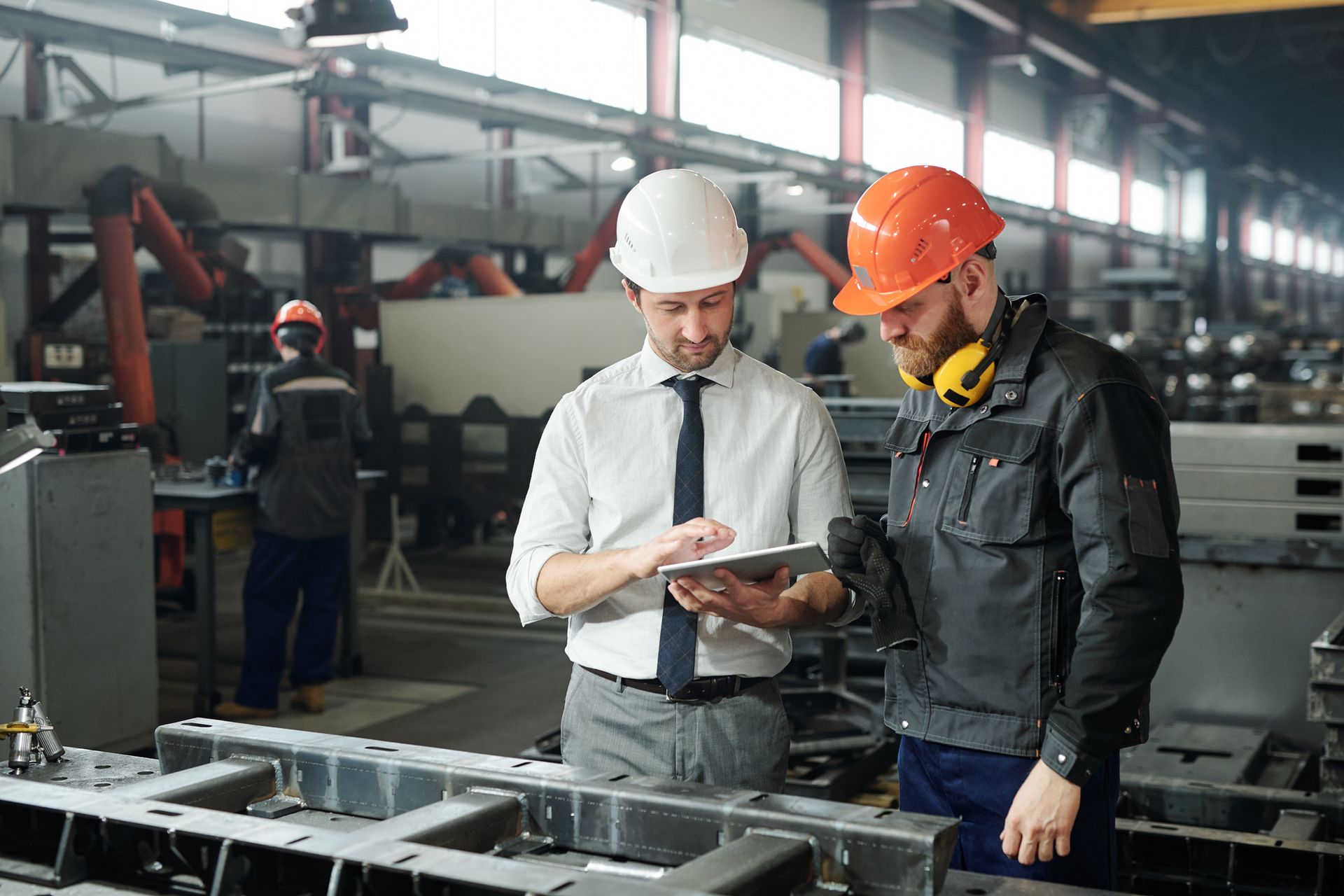 Two men in hard hats looking at tablet in factory setting.