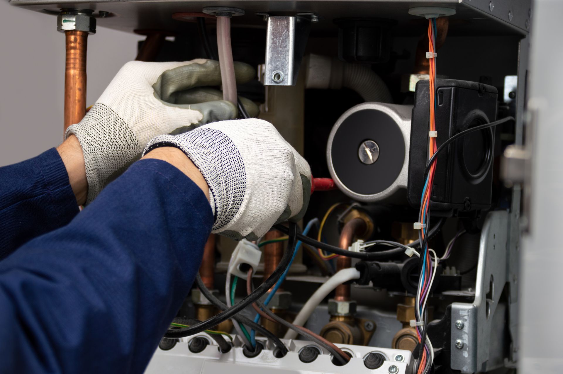 Hands wearing work gloves repairing a boiler's internal components. 