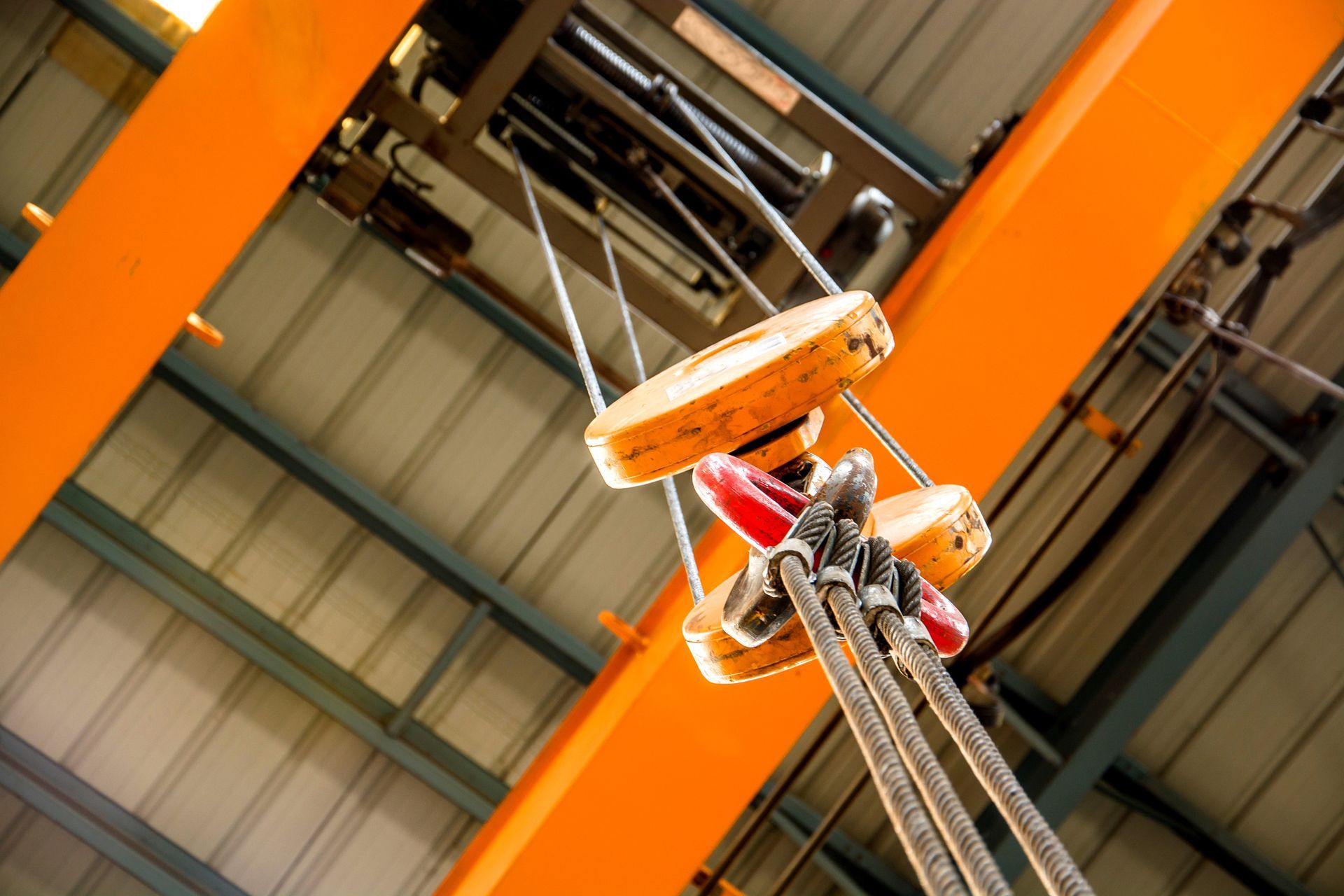 Overhead crane, orange beams and pulleys, cables hanging.