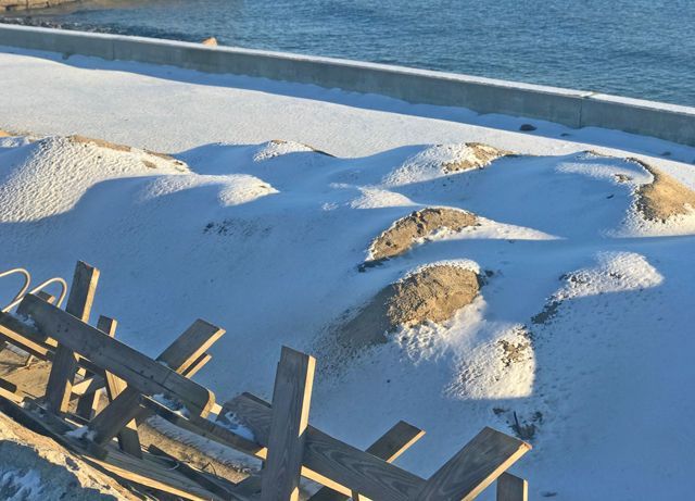 Snow-covered area beside water with wooden beams in the foreground