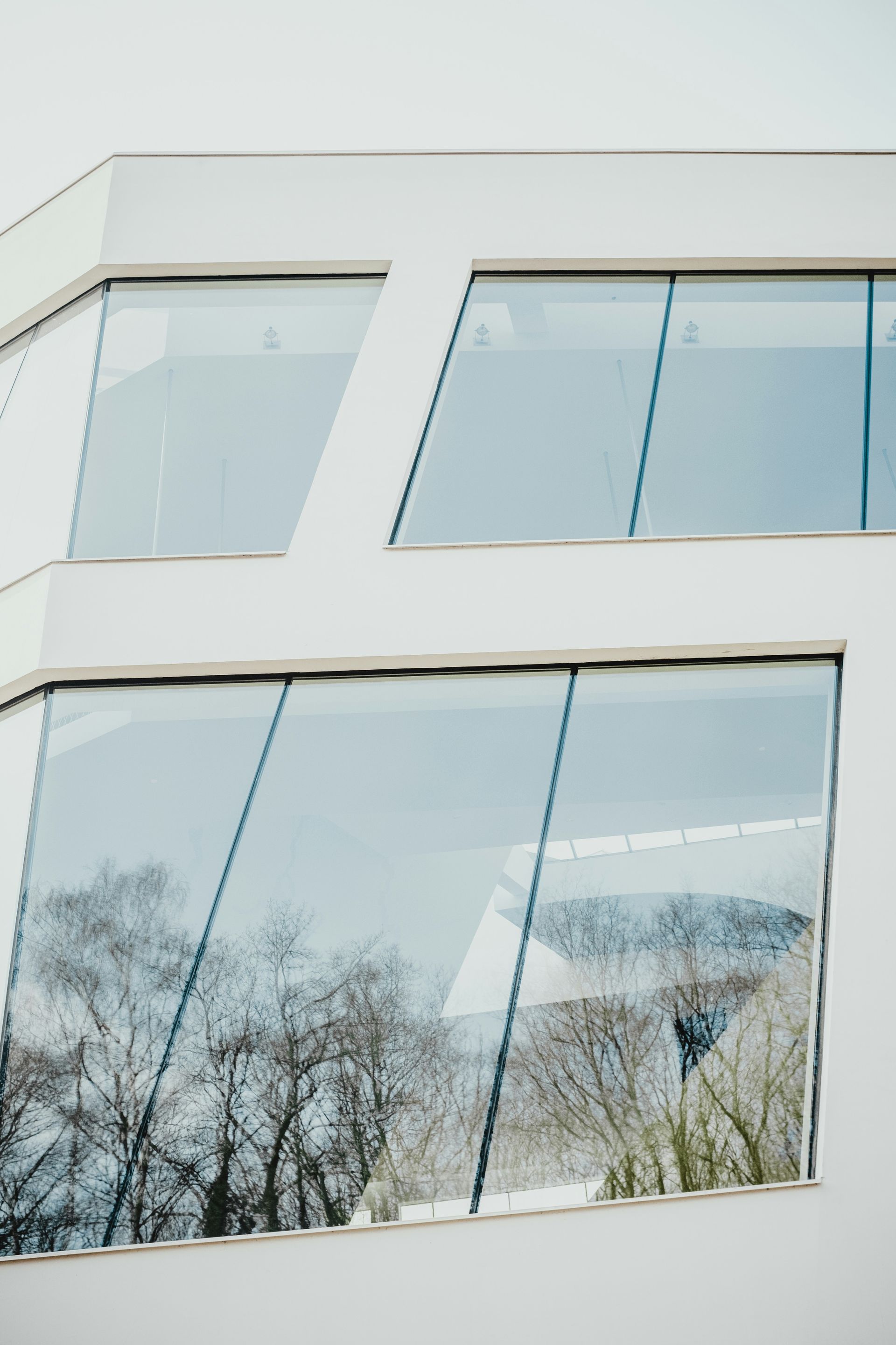 A white building with a lot of windows and trees reflected in the windows.