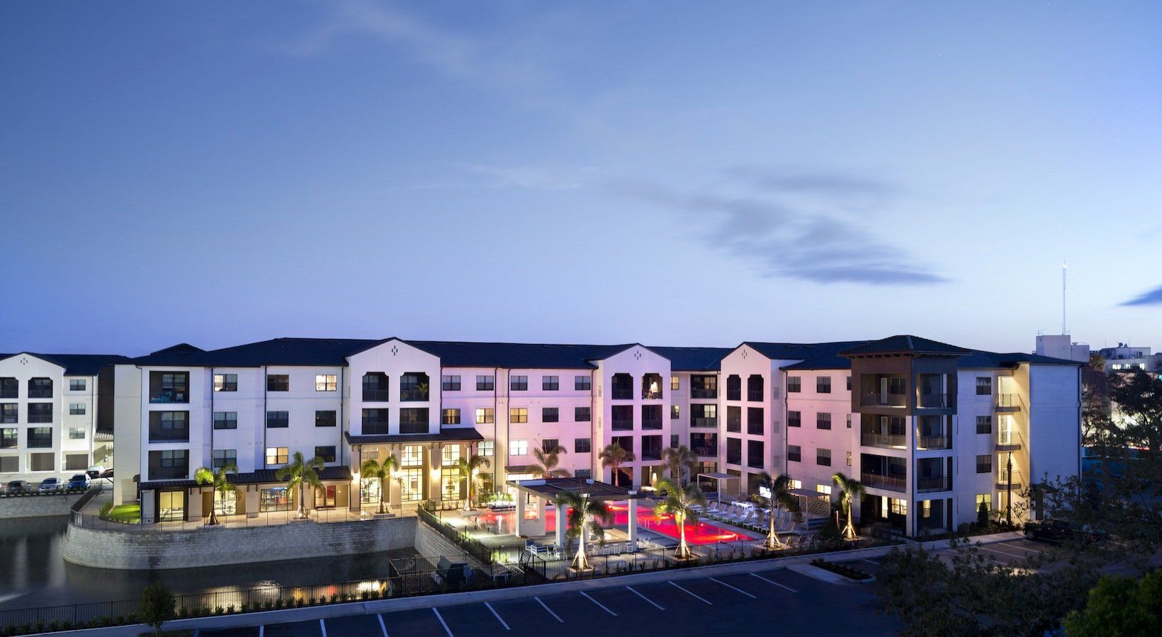 Apartment building at dusk with pool and pond.