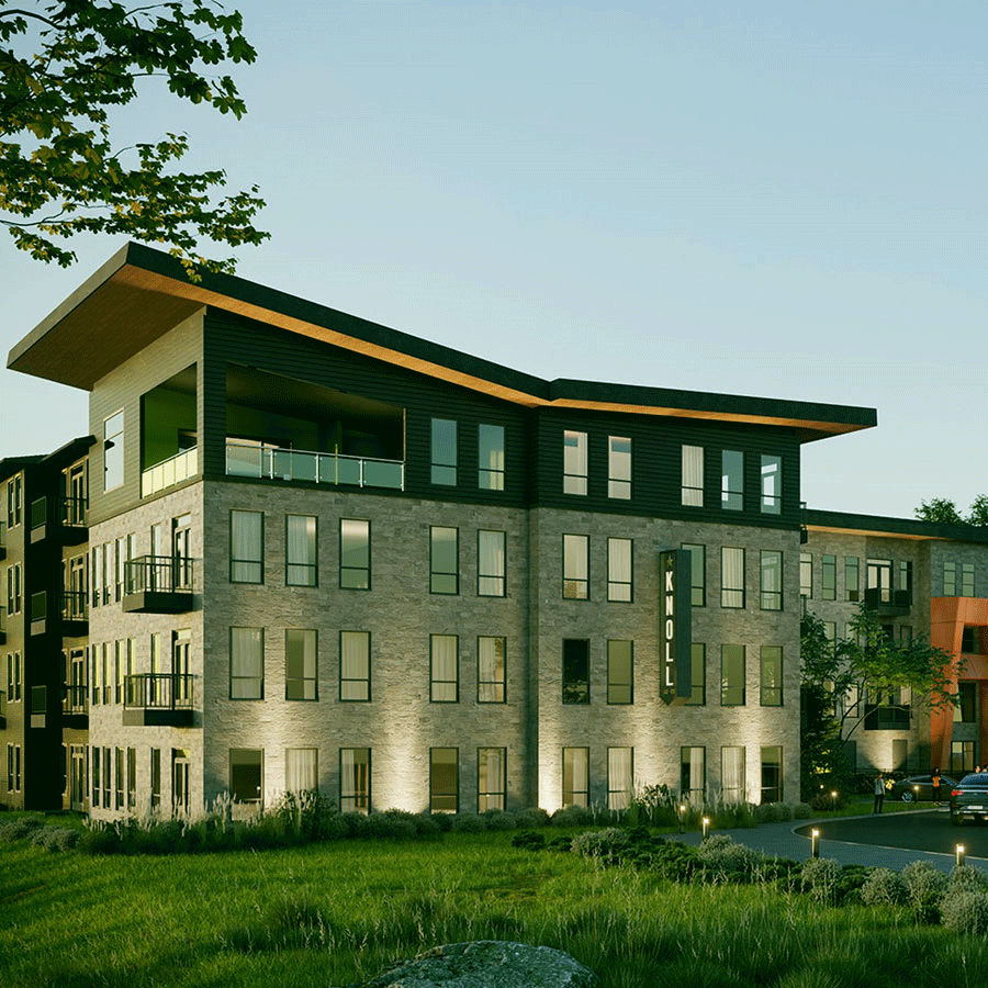 Multi-story brick building with large windows, green lawn, and angled rooftop under blue sky.