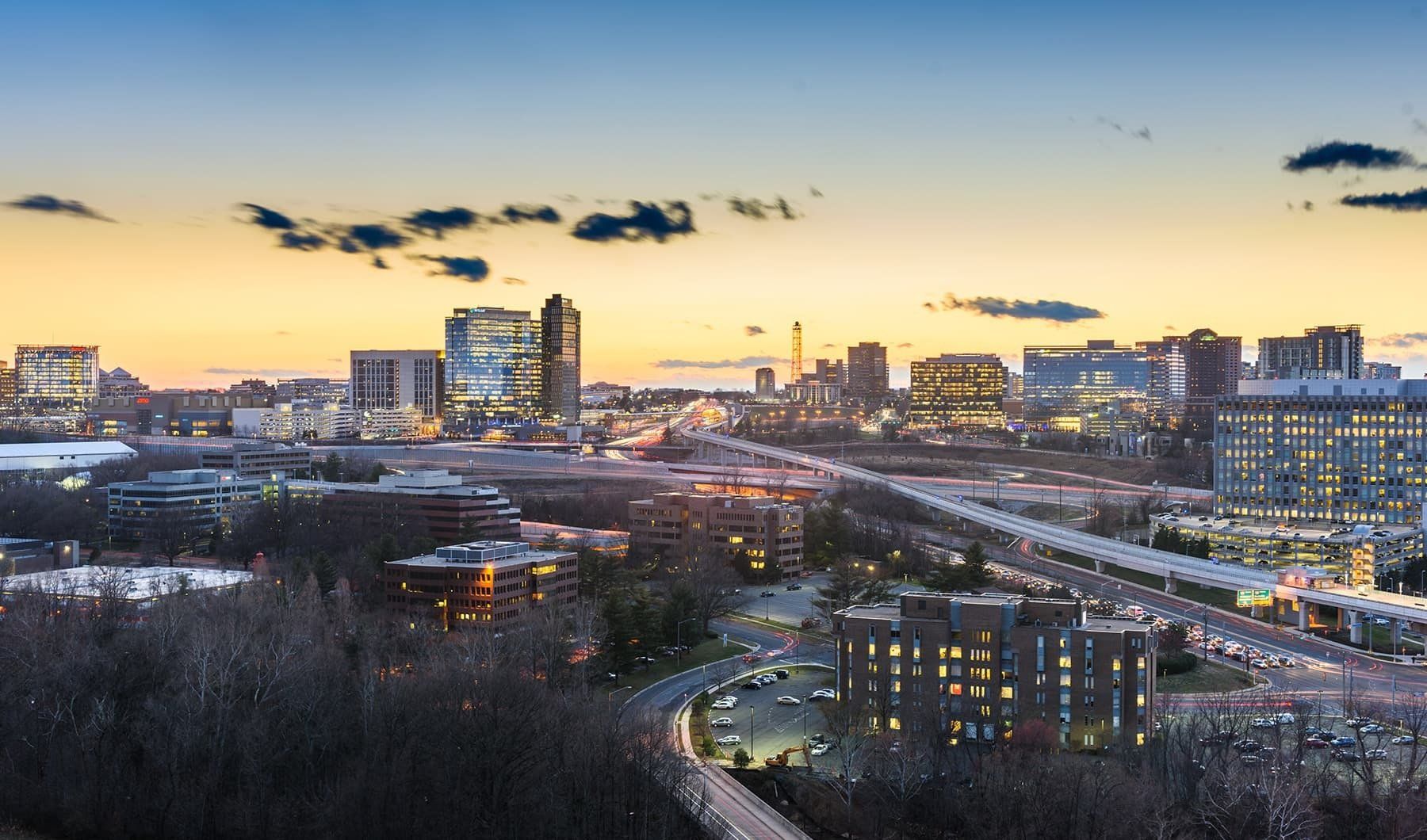 Skyline of Arlington, Virginia at dusk, with buildings and roadways illuminated against a colorful sky.