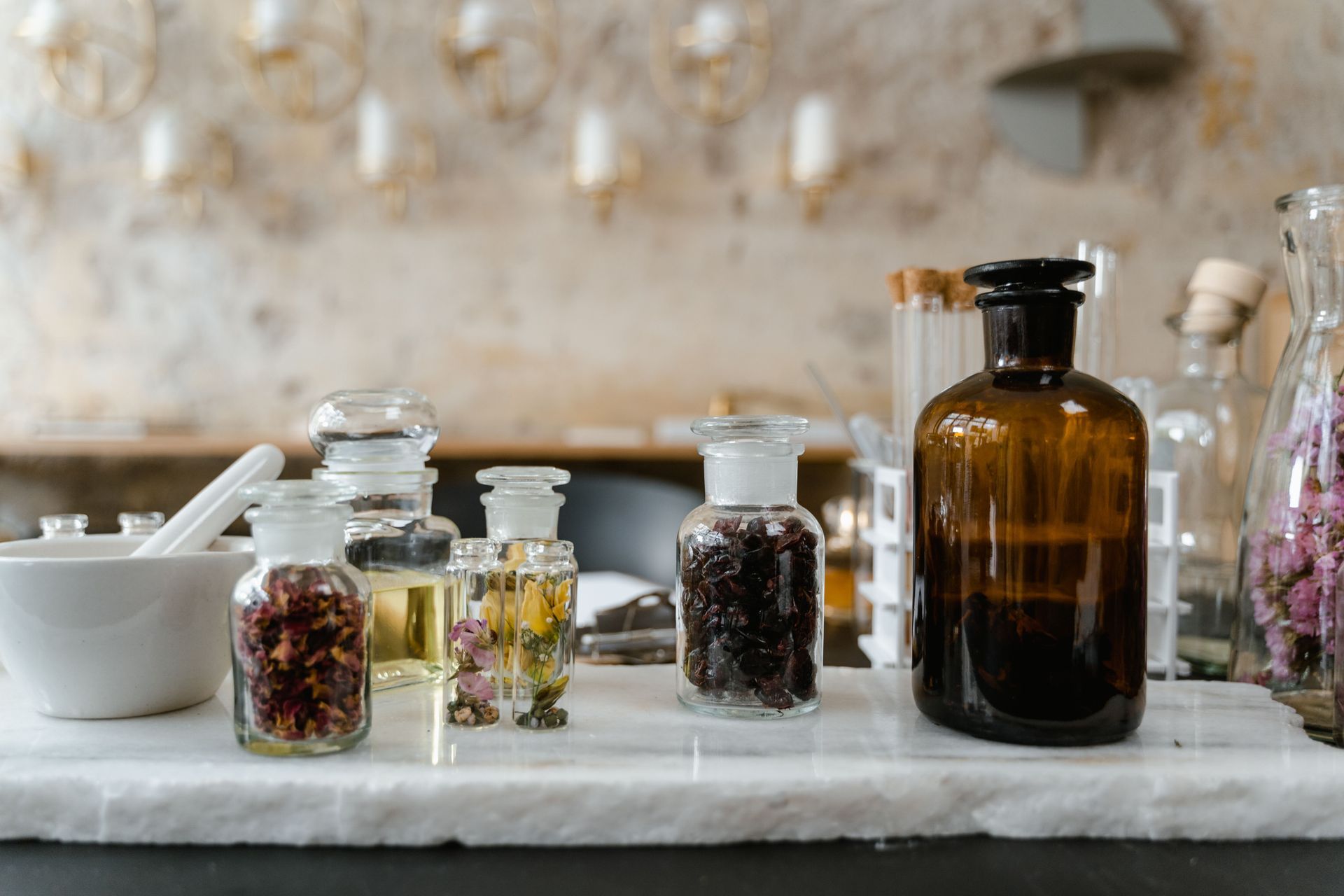 Assorted glass jars and bottles of herbs and liquids on a marble counter in a rustic kitchen